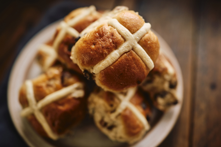 Overhead view of a plate of Hot Cross Buns on a rustic dark wooden table top.